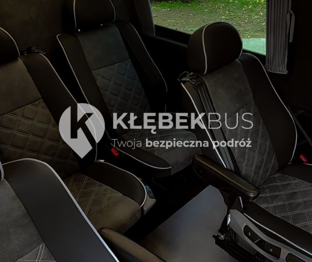 Wnętrze luksusowego busa z czarno-szarą tapicerką w romby, logo firmy KłębekBus na siedzeniu.