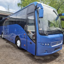 BTT Polska - Niebieski autobus marki Volvo po odnowieniu lakieru, stojący na placu przed budynkiem warsztatowym z otwartymi wrotami, widoczny skuter w tle.