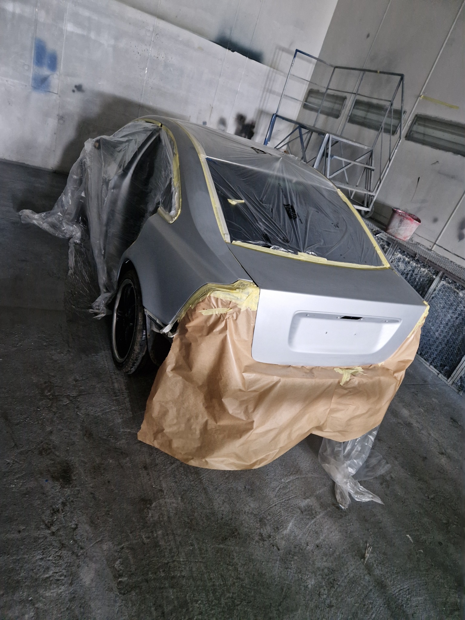 Samochód osobowy przygotowany do lakierowania, zabezpieczony folią i papierem maskującym, widoczny w warsztacie.