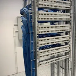 Panel krosowniczy z uporządkowanymi niebieskimi kablami sieciowymi w metalowej szafie rack, widoczne porty RJ45 z numeracją.