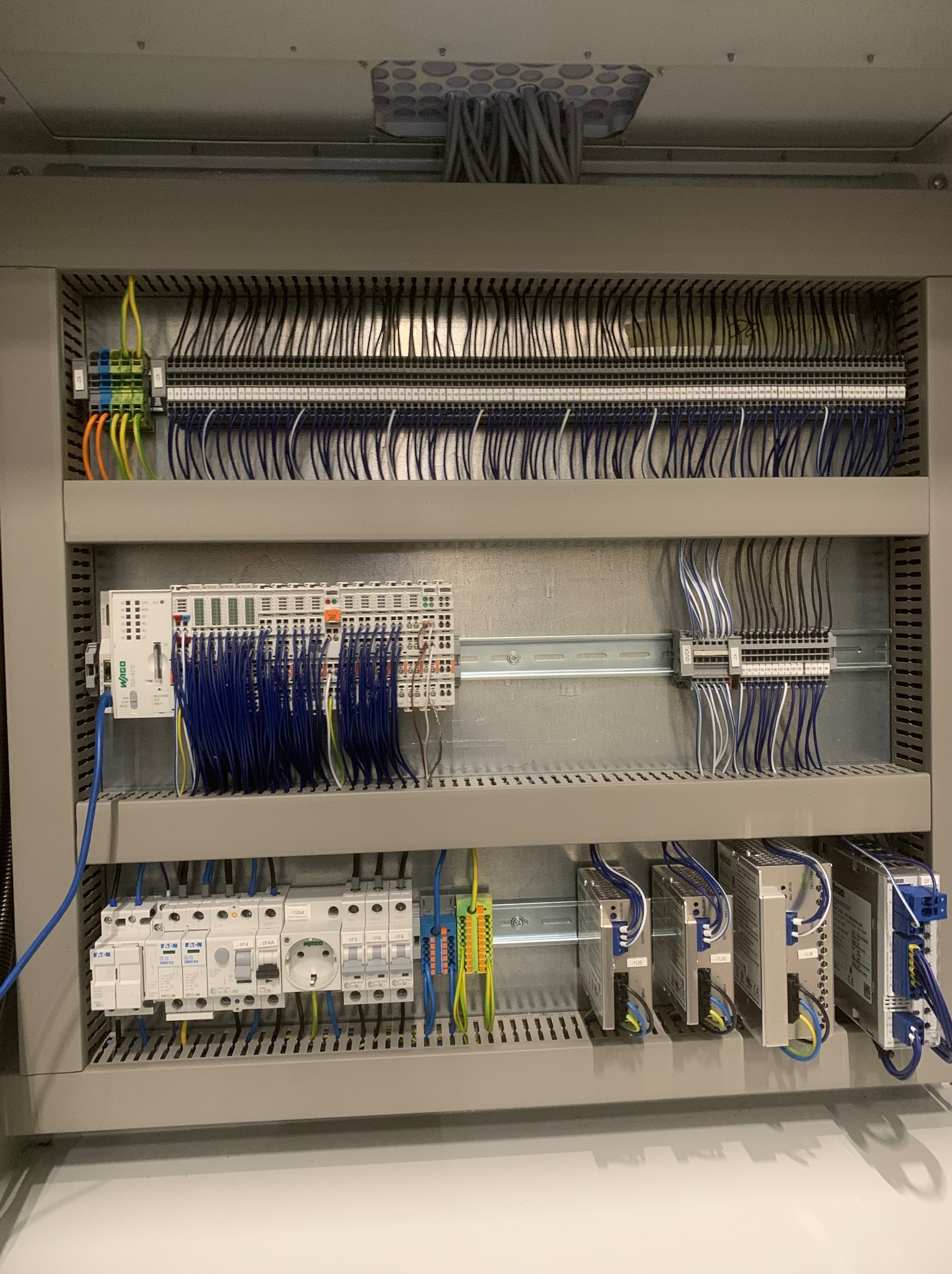 Szczegółowe ujęcie rozdzielnicy elektrycznej z licznymi przewodami, modułami WAGO i zabezpieczeniami Eaton, ukazujące profesjonalny montaż w szarej obudowie.