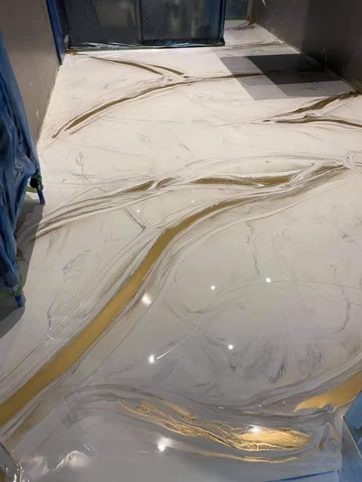 Biała posadzka z żywicy epoksydowej imitująca marmur, z płynnymi, złotymi żyłkami, świeżo wylana, z widocznym niebieskim zabezpieczeniem ścian.
