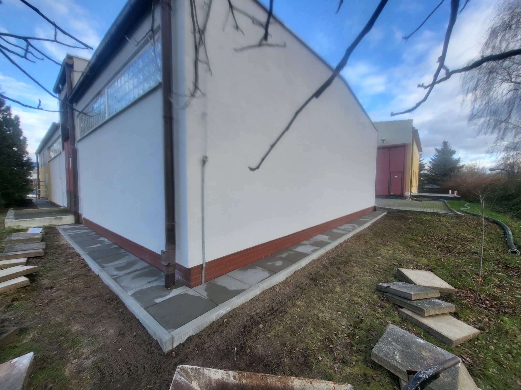 Świeżo ułożona kostka brukowa przy budynku w Szczecinie, z widocznymi płytami czekającymi na montaż. Jasne niebo w tle, surowy krajobraz.