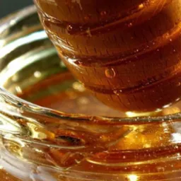 Zbliżenie na słoik z bursztynowym płynem i zanurzony w nim drewniany nabierak, kropla spływa z nabieraka.