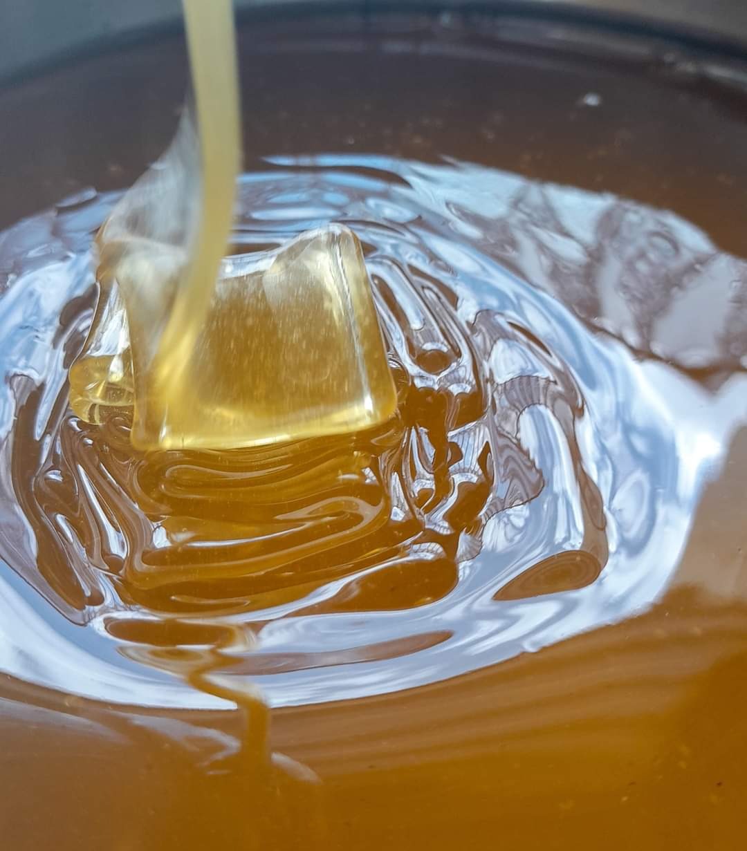 Strumień bursztynowego płynu wlewa się do naczynia, tworząc wirujące wzory na powierzchni.