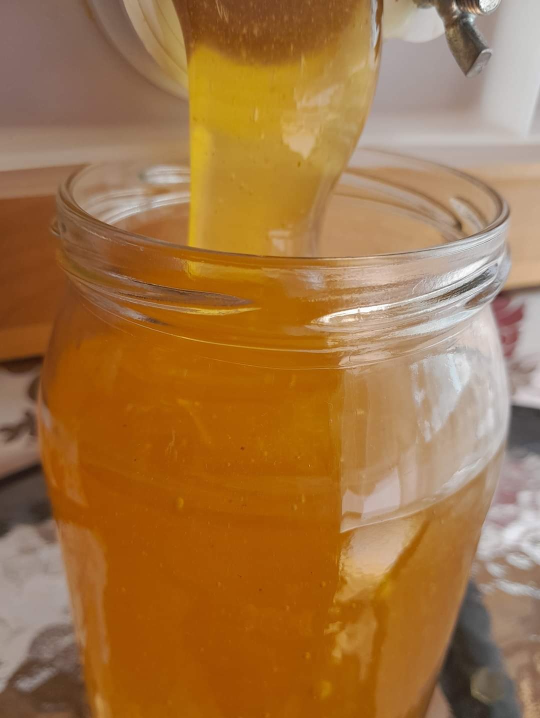 Gęsty, bursztynowy miód spływa z kranu do szklanego słoika, wypełniając go niemal po brzeg.