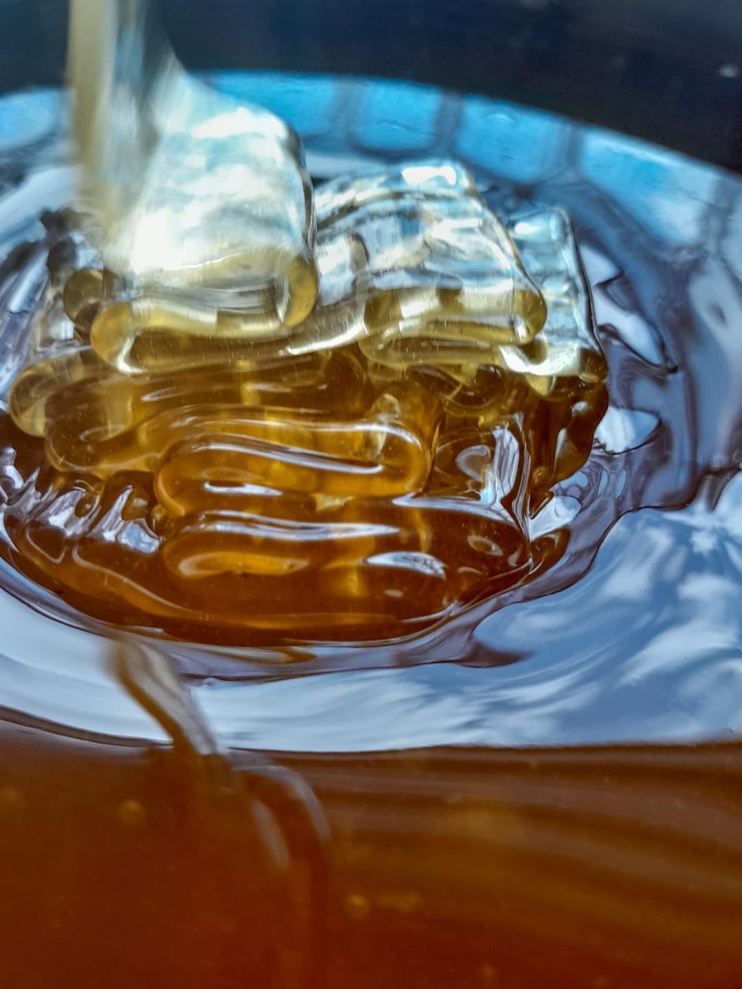 Strumień gęstego, bursztynowego płynu spływa do naczynia, tworząc warstwy o różnej konsystencji i odcieniach brązu.
