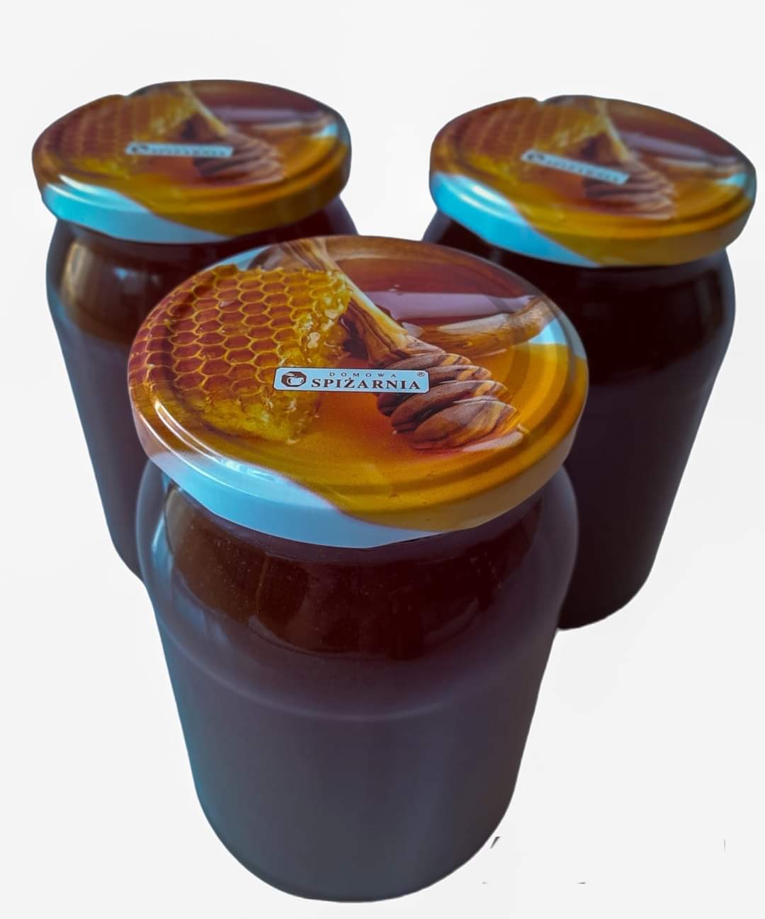Trzy słoiki ciemnego miodu z etykietą 'Domowa Spiżarnia' na wieczkach, ustawione w trójkąt na białym tle.