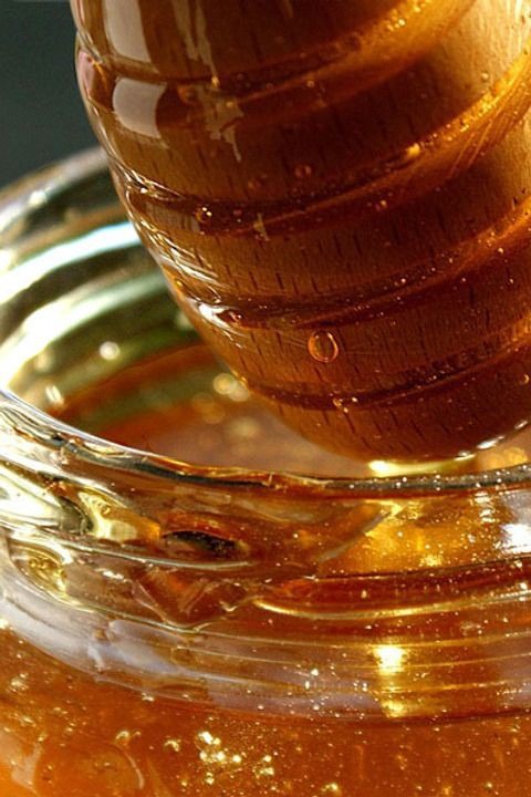 Zbliżenie na słoik z bursztynowym płynem i zanurzony w nim drewniany nabierak, kropla spływa z nabieraka.