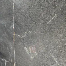 Zbliżenie na szarą, teksturowaną powierzchnię z delikatnymi żyłkami przypominającymi marmur, możliwe fragment płyty lub panelu.