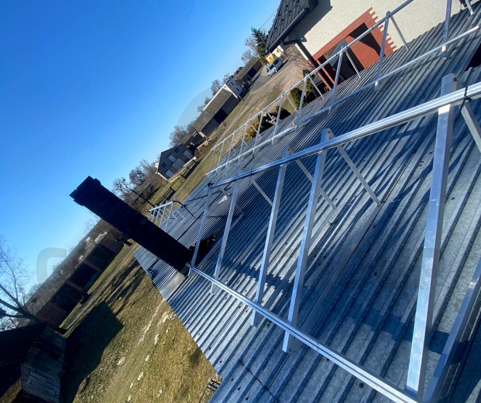 Metalowa konstrukcja rusztowania na falistym dachu budynku jednorodzinnego, widok z dołu pod kątem w słoneczny dzień.