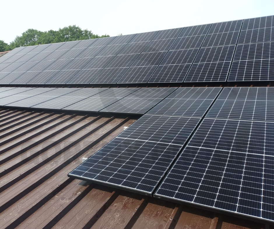 Panele słoneczne zamontowane na metalowym dachu z widocznymi drzewami w tle, ujęcie z niskiego kąta.