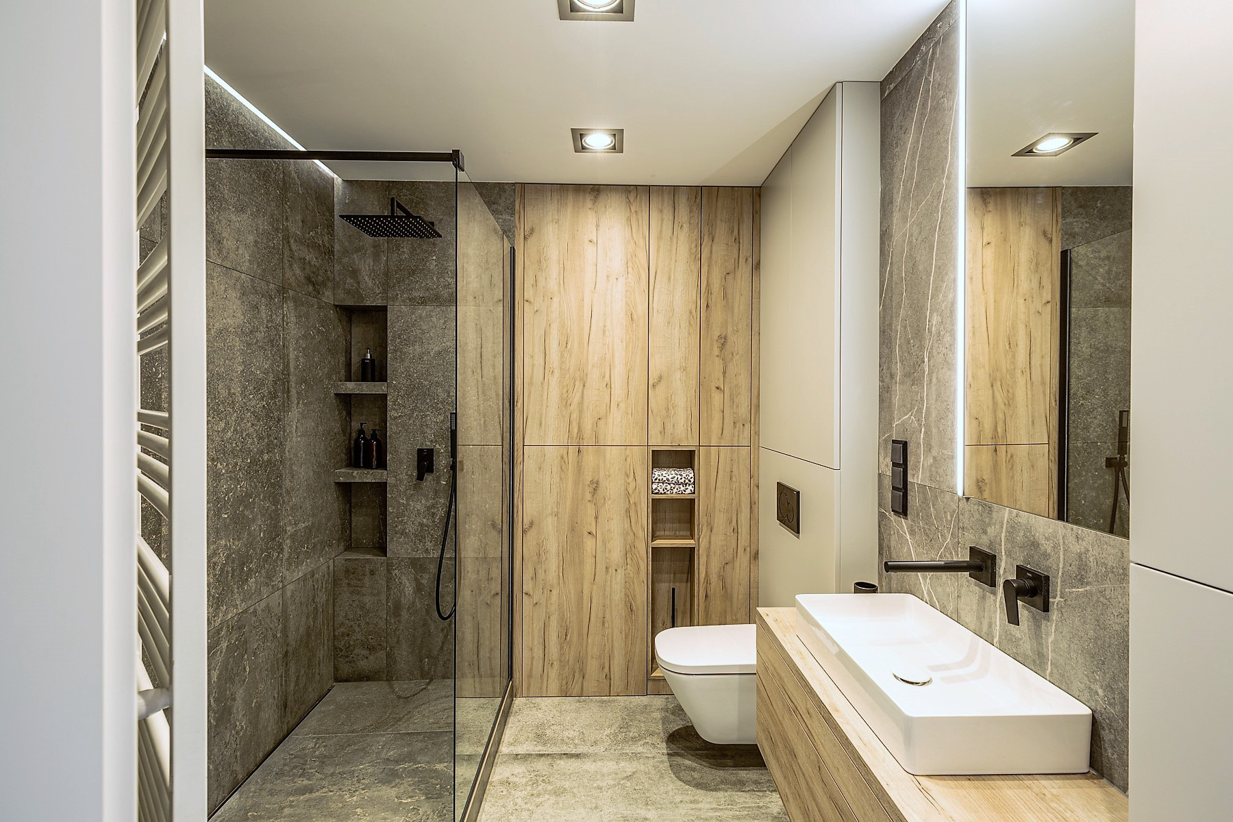 Nowoczesna łazienka z kabiną prysznicową typu walk-in, wykończona płytkami imitującymi kamień i drewnem, z czarną armaturą i oświetleniem LED.