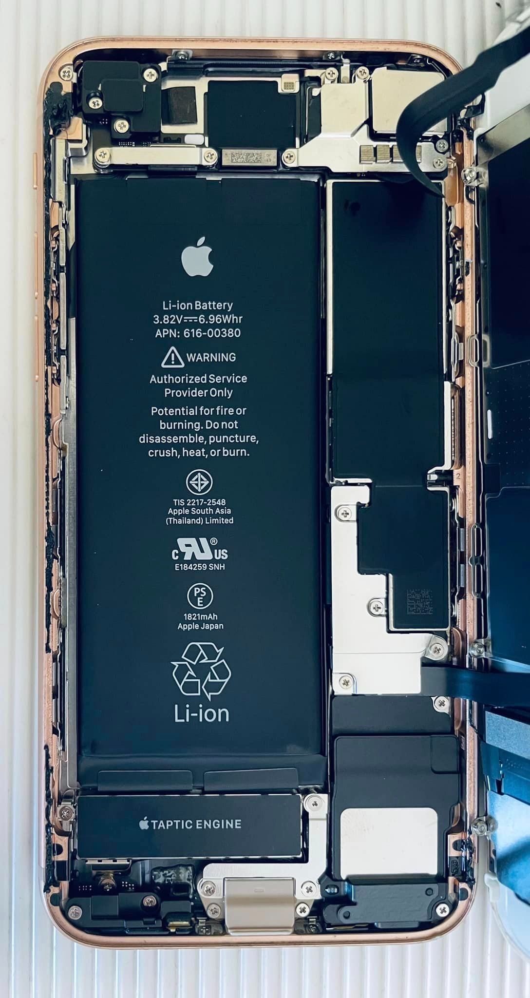 Wnętrze rozłożonego iPhone'a z widoczną baterią, modułem Taptic Engine i elementami konstrukcyjnymi w kolorze różowego złota.