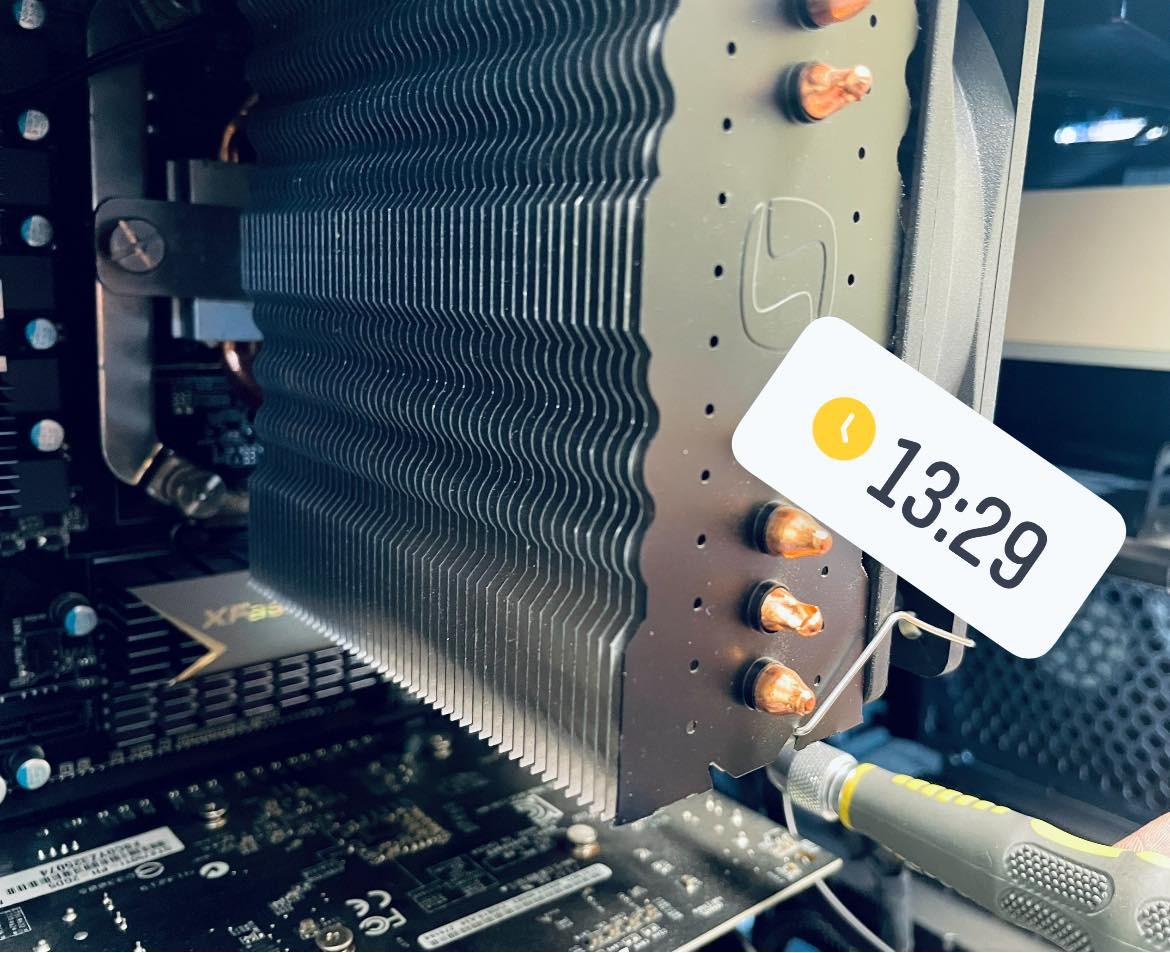 Detale montażu chłodzenia procesora z radiatorem i heatpipe'ami w komputerze stacjonarnym, widoczna płyta główna i narzędzie monterskie.