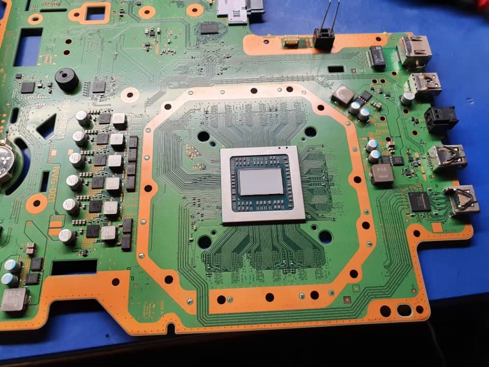 Płyta główna konsoli do gier z widocznym procesorem centralnym, portami USB i elementami elektronicznymi na niebieskim tle.