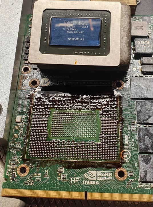 Zdjęcie płyty głównej komputera z widocznym układem scalonym NVIDIA N12E-Q1-A1, z naniesioną pastą termoprzewodzącą i elementami elektronicznymi w tle.