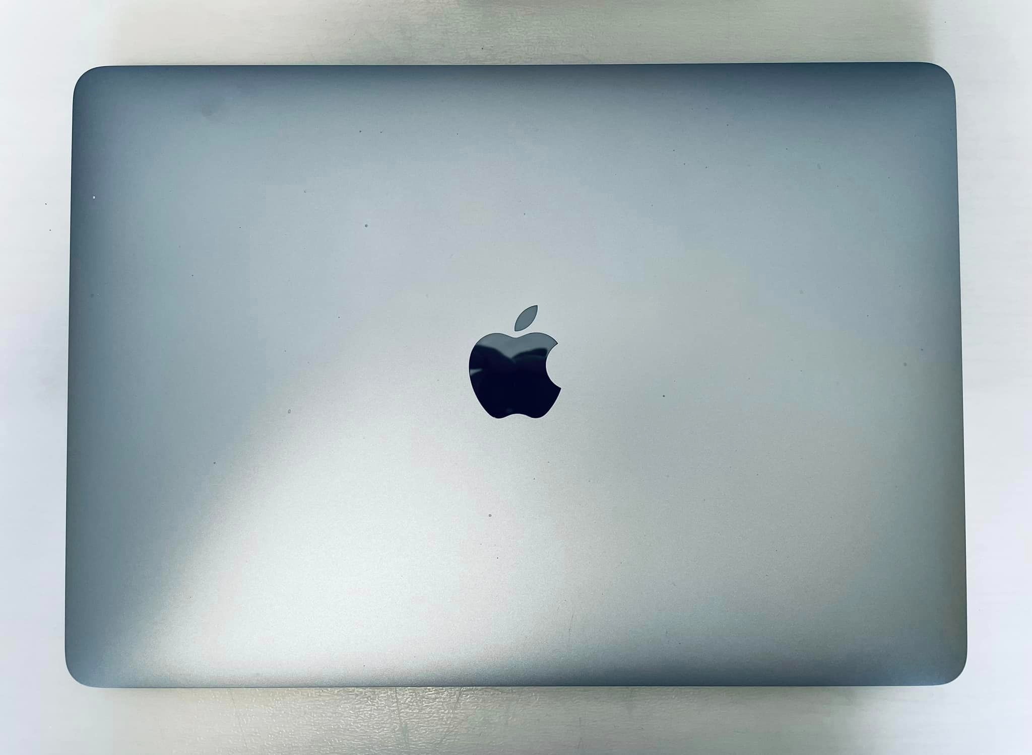 Zamknięty, srebrny laptop Apple MacBook z widocznym logo na obudowie, leżący na białym tle.
