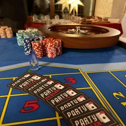 Party Dealer - Stół do ruletki z żetonami i kartami 'Party Dealer' na imprezie. W tle dekoracja w kształcie gwiazdy. Całość w ciepłym oświetleniu.