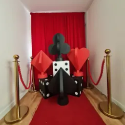 Kreatywna fotobudka z motywem kasyna: czerwony dywan, złote słupki, gigantyczne karty i kostki do gry. Idealna na imprezy tematyczne i eventy.