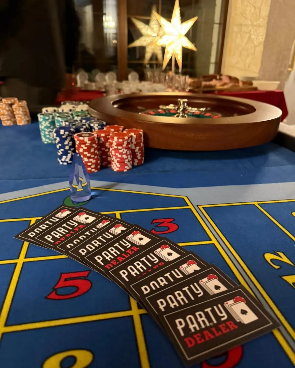 Stół do ruletki z żetonami i kartami 'Party Dealer' na imprezie. W tle dekoracja w kształcie gwiazdy. Całość w ciepłym oświetleniu.