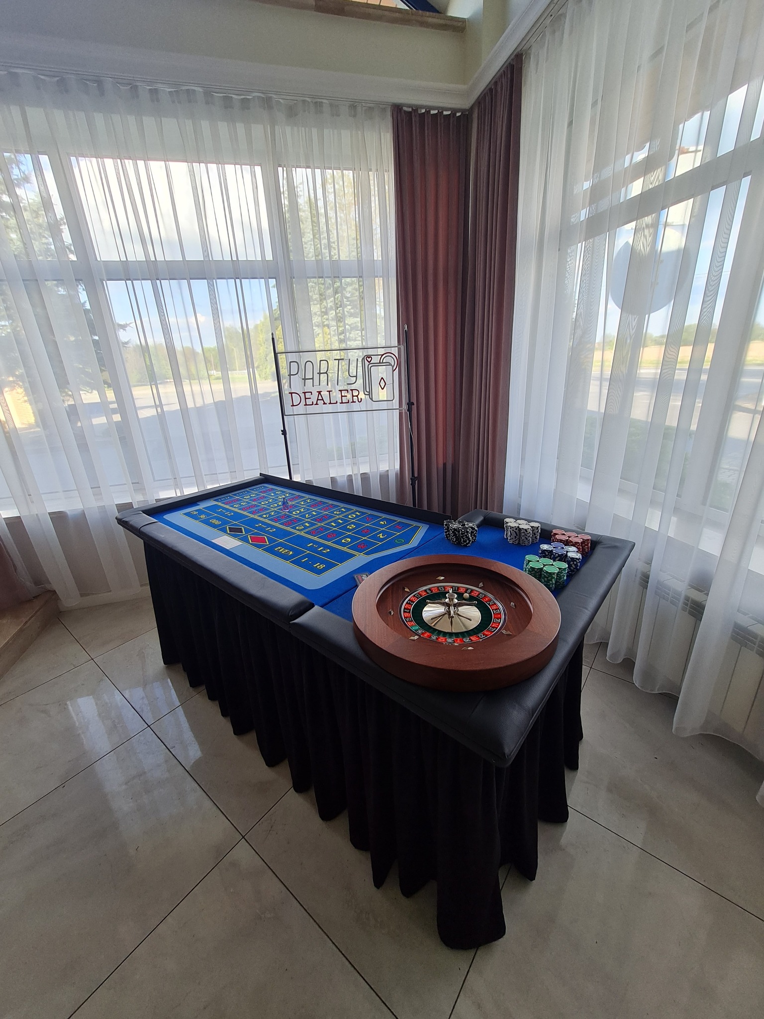 Stół do ruletki z żetonami i napisem 'Party Dealer' w Katowicach, ustawiony w jasnym pomieszczeniu z oknami i zasłonami, gotowy do imprezy tematycznej.