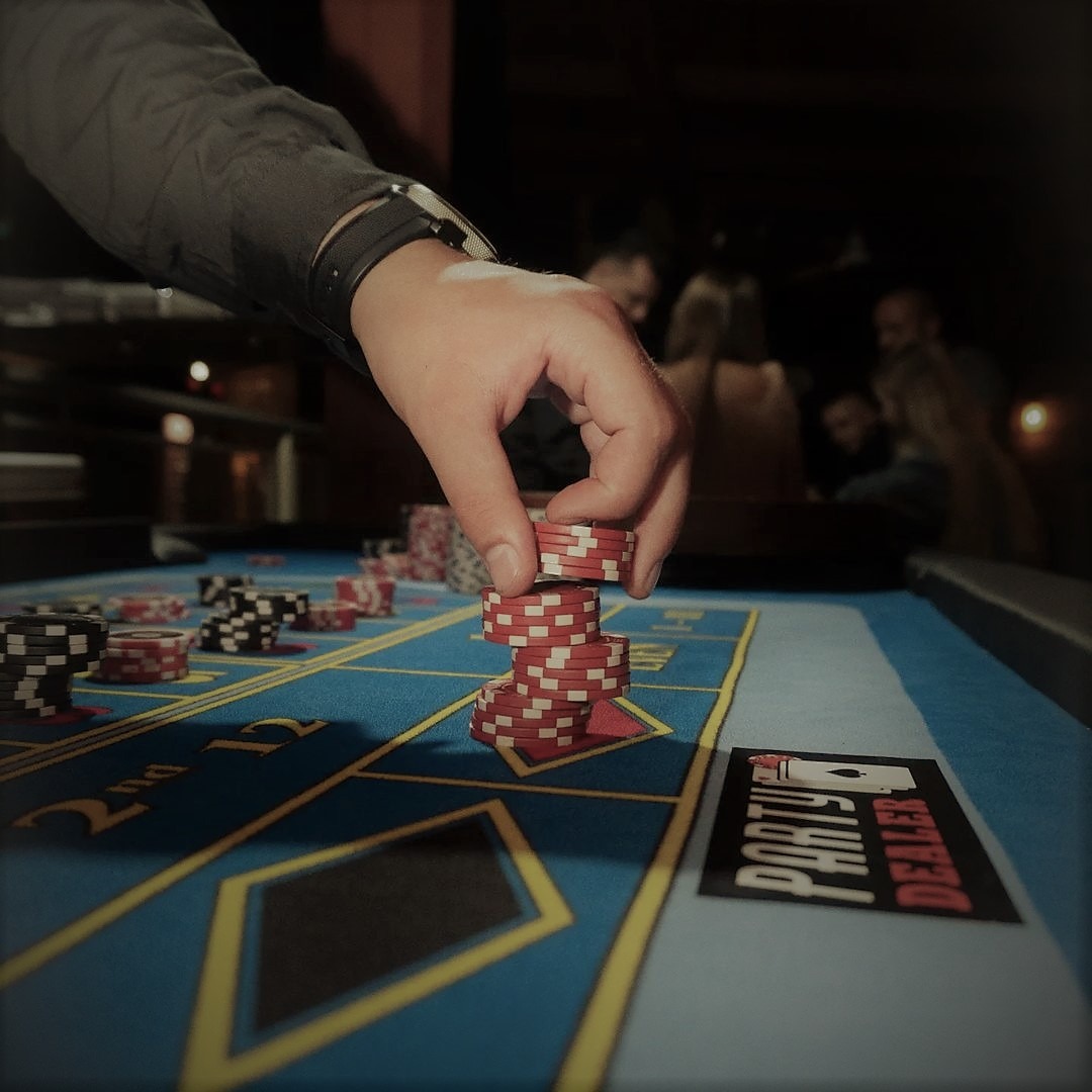 Układanie żetonów na stole do gry w kasynie, w tle widoczni gracze, na stole leży wizytówka z logo.