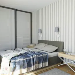 Nowoczesna sypialnia z łóżkiem, szafą przesuwną z mlecznego szkła, tapetą w szaro-białe pasy i designerską szafką nocną na metalowych nogach.