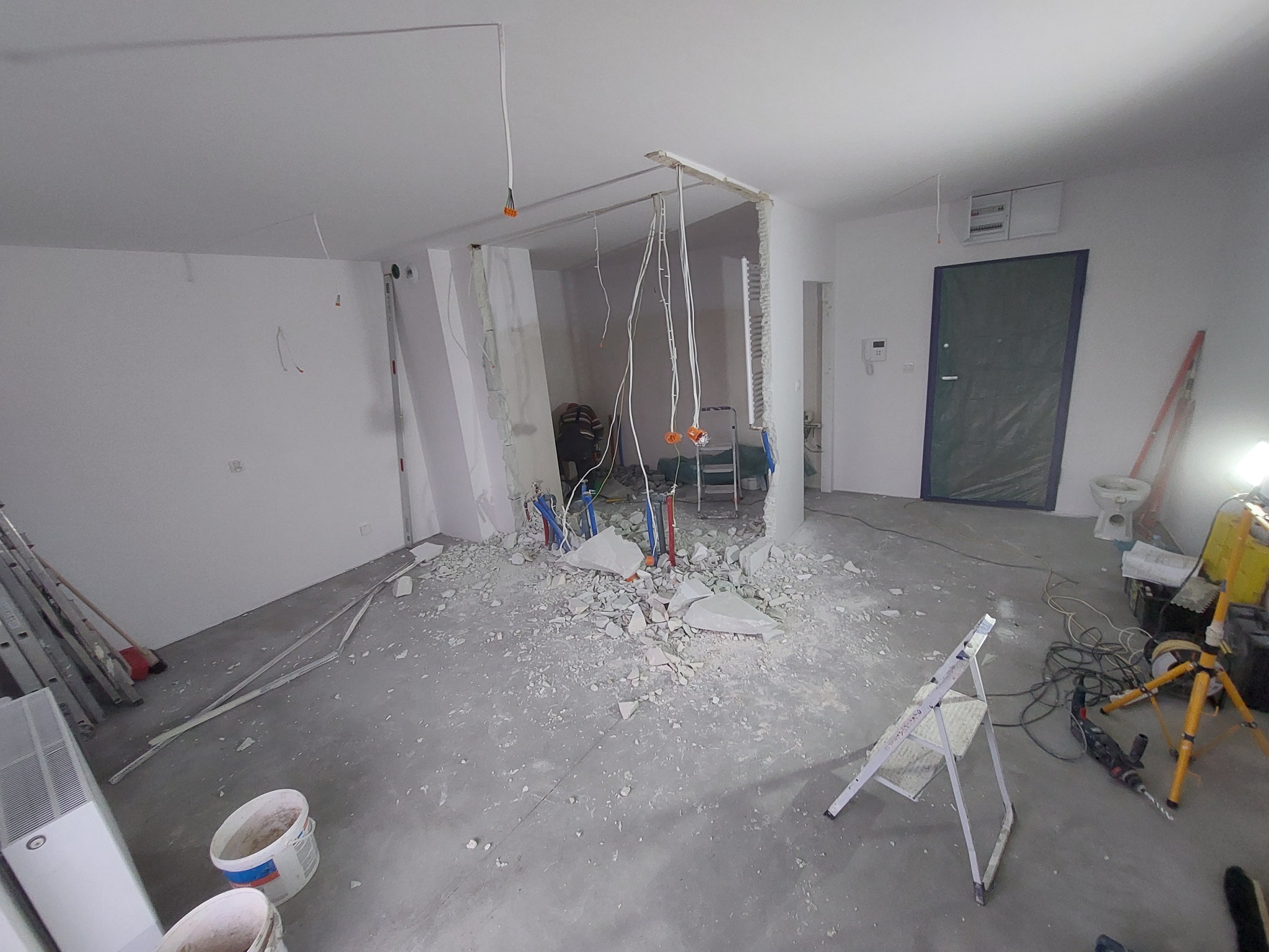 Demontaż ściany działowej w trakcie remontu, widoczne instalacje wodne, gruz, drabina i narzędzia.