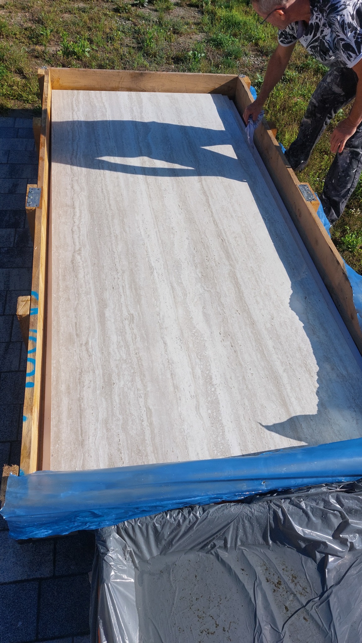 Przygotowanie formy z drewnianych desek, wyłożonej folią, do wylania posadzki z beżowego trawertynu z widocznym wzorem słojów.