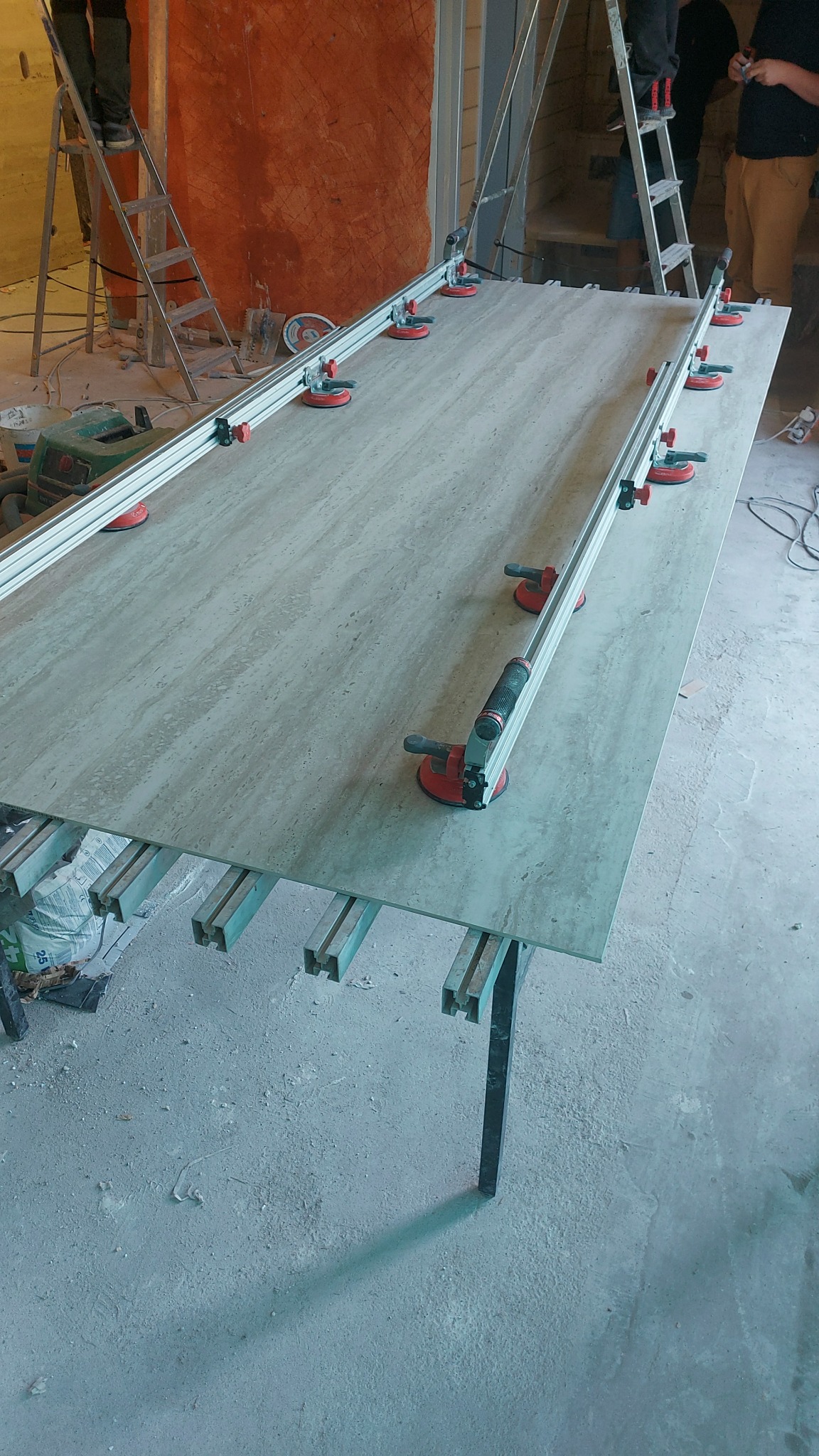 Przygotowanie do cięcia płyty trawertynowej z użyciem przyssawkowej prowadnicy w trakcie prac wykończeniowych we Wrocławiu. Widoczne narzędzia, drabina i fragment ściany z fakturą.