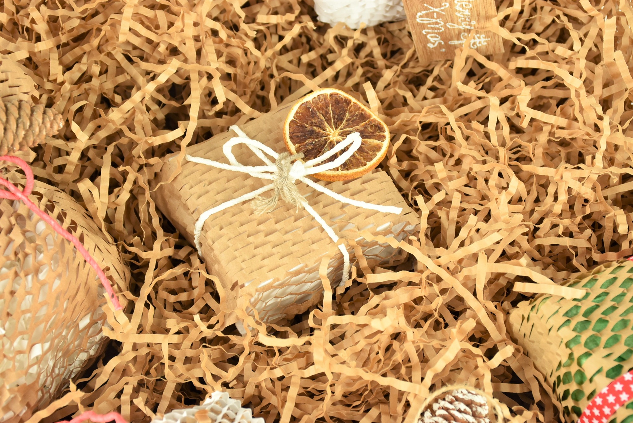 Prezent zapakowany w tekturowe opakowanie i ozdobiony suszoną pomarańczą, otoczony wypełniaczem z pociętego papieru w Łękach.