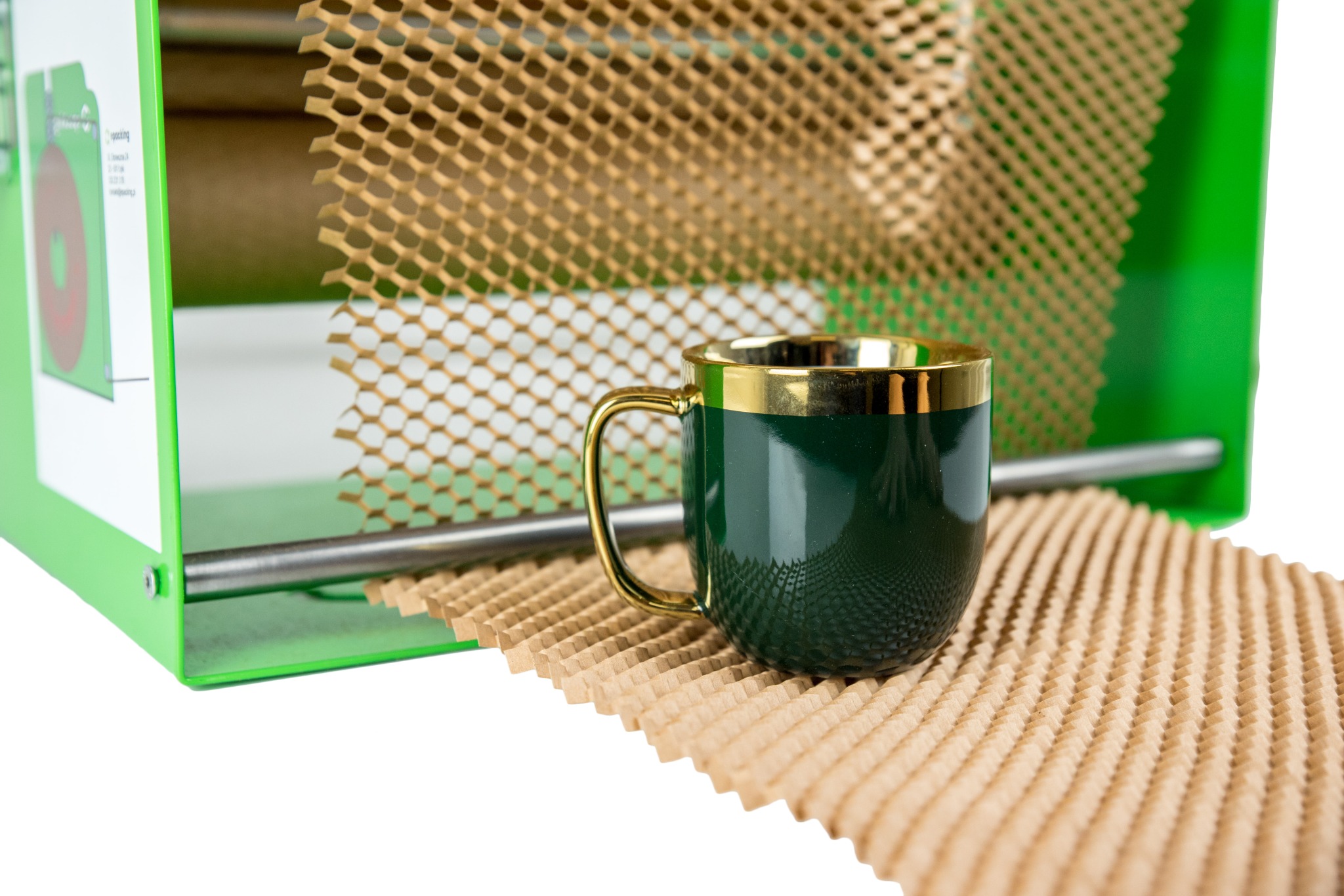 Zielony kubek z złotym obramowaniem na tle rozciągniętej papierowej siatki o strukturze plastra miodu, wychodzącej z zielonego dyspensera do wypełniania przestrzeni w paczkach.