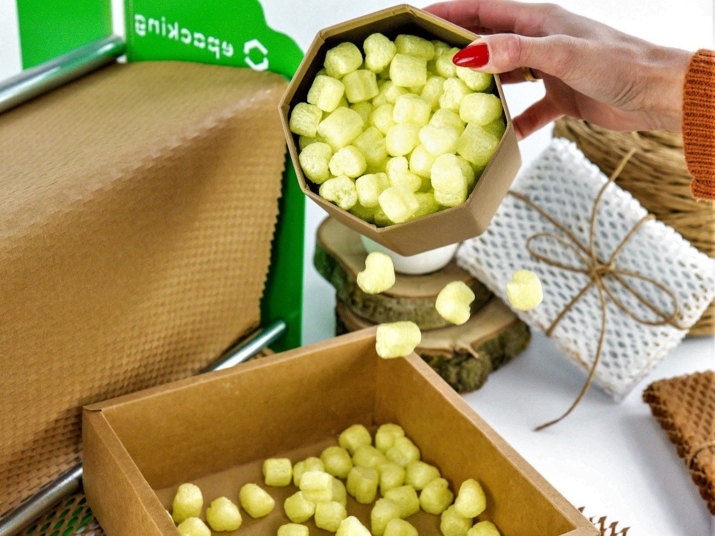 Wypełniacze do paczek z bio pianki w kartonowych pojemnikach o różnej fakturze, uzupełniane ręcznie, z widocznymi elementami dekoracyjnymi pakowania.