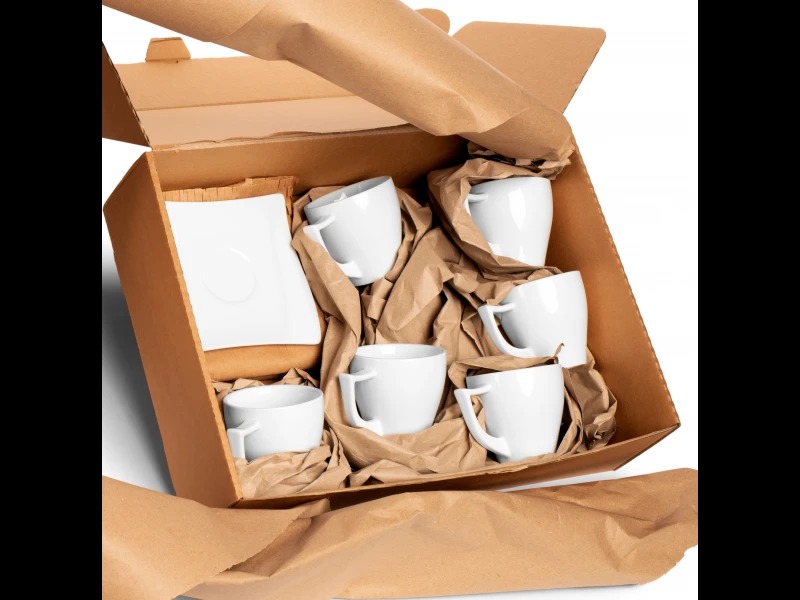 Kartonowe pudełko wypełnione brązowym papierem i białymi filiżankami z kwadratowym spodkiem.