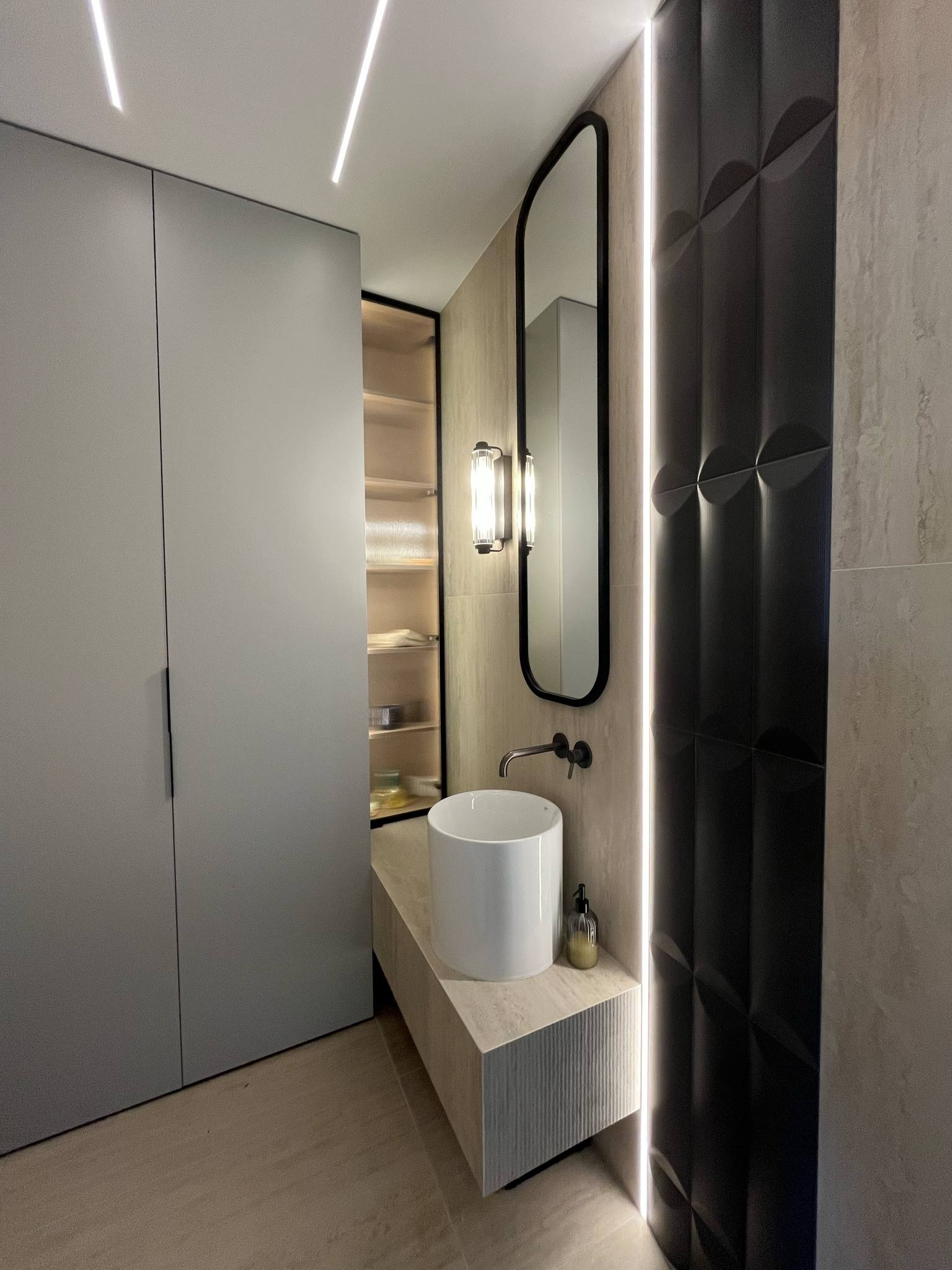 Nowoczesna łazienka z szafką, umywalką nablatową i podświetlanym lustrem. Ciemne panele ścienne z geometrycznym wzorem i ledowe oświetlenie akcentujące.