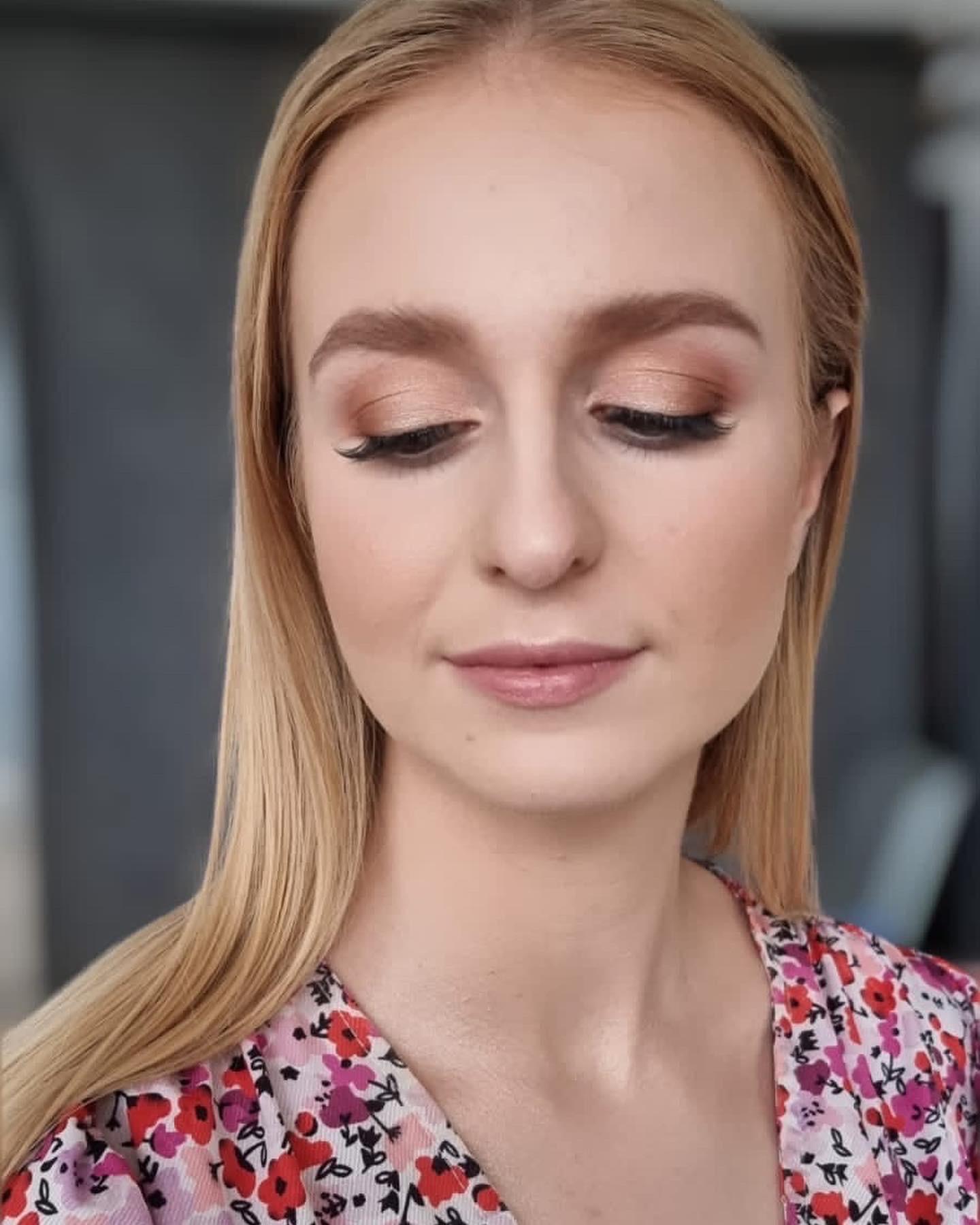 Portret kobiety z delikatnym, brzoskwiniowym cieniem na powiekach, sztucznymi rzęsami i błyszczącymi ustami, ubrana w bluzkę w kwiaty