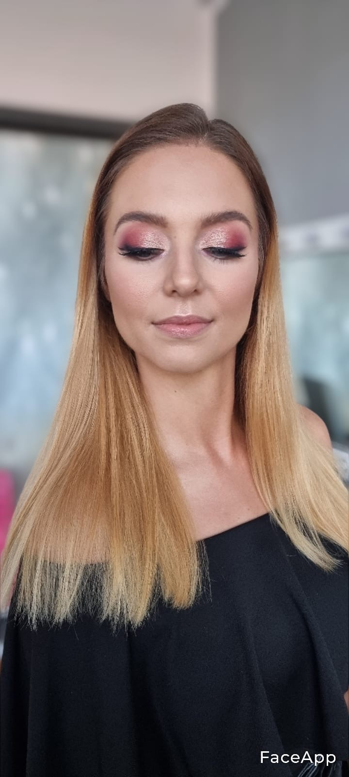 Portret kobiety z blond włosami i delikatnym, błyszczącym różowo-złotym cieniowaniem powiek oraz wydłużonymi rzęsami, ubrana w czarną bluzkę z odkrytym ramieniem.