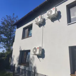 Elewacja domu z trzema zamontowanymi klimatyzatorami TCL, połączonymi rurami. Widok z dołu, błękitne niebo w tle. Instalacja klimatyzacji zewnętrznej.