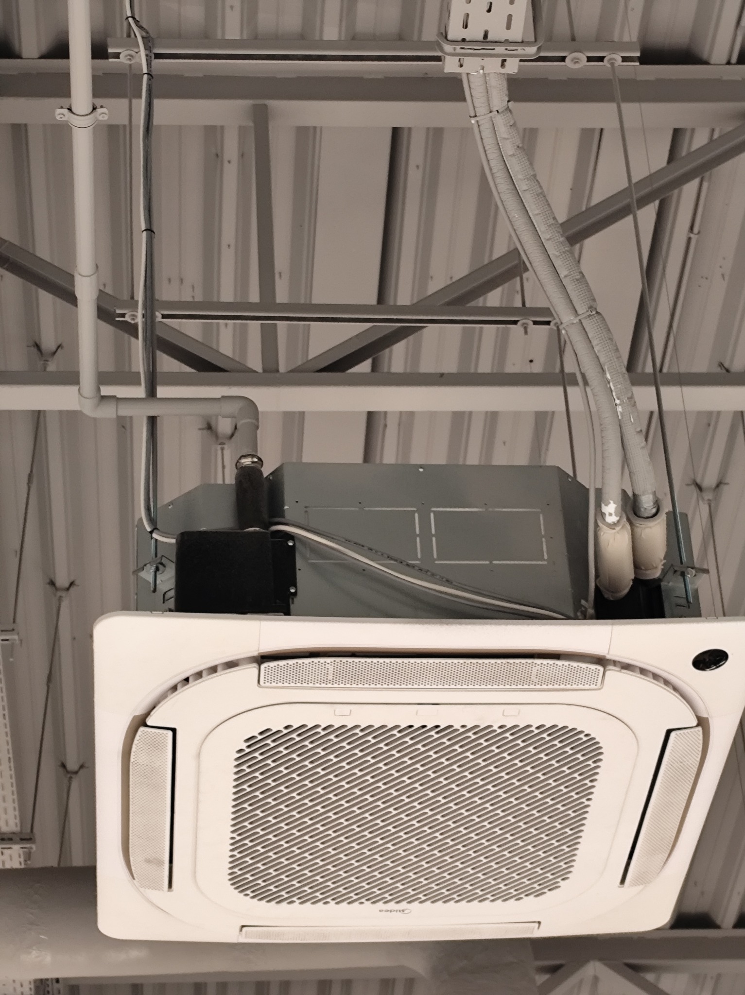 Kasetonowa klimatyzacja sufitowa z widocznymi przewodami w Mielcu. Biała obudowa, kratka wentylacyjna. Widok od dołu, instalacja w hali.