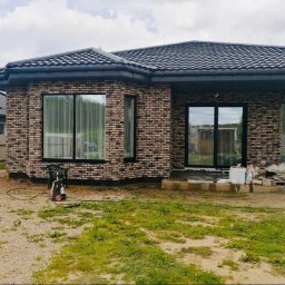 Blok.cz - Nowo wybudowany dom z cegły klinkierowej z czarnymi oknami i dachem, na zewnątrz widoczny sprzęt do czyszczenia ciśnieniowego i materiały budowlane.