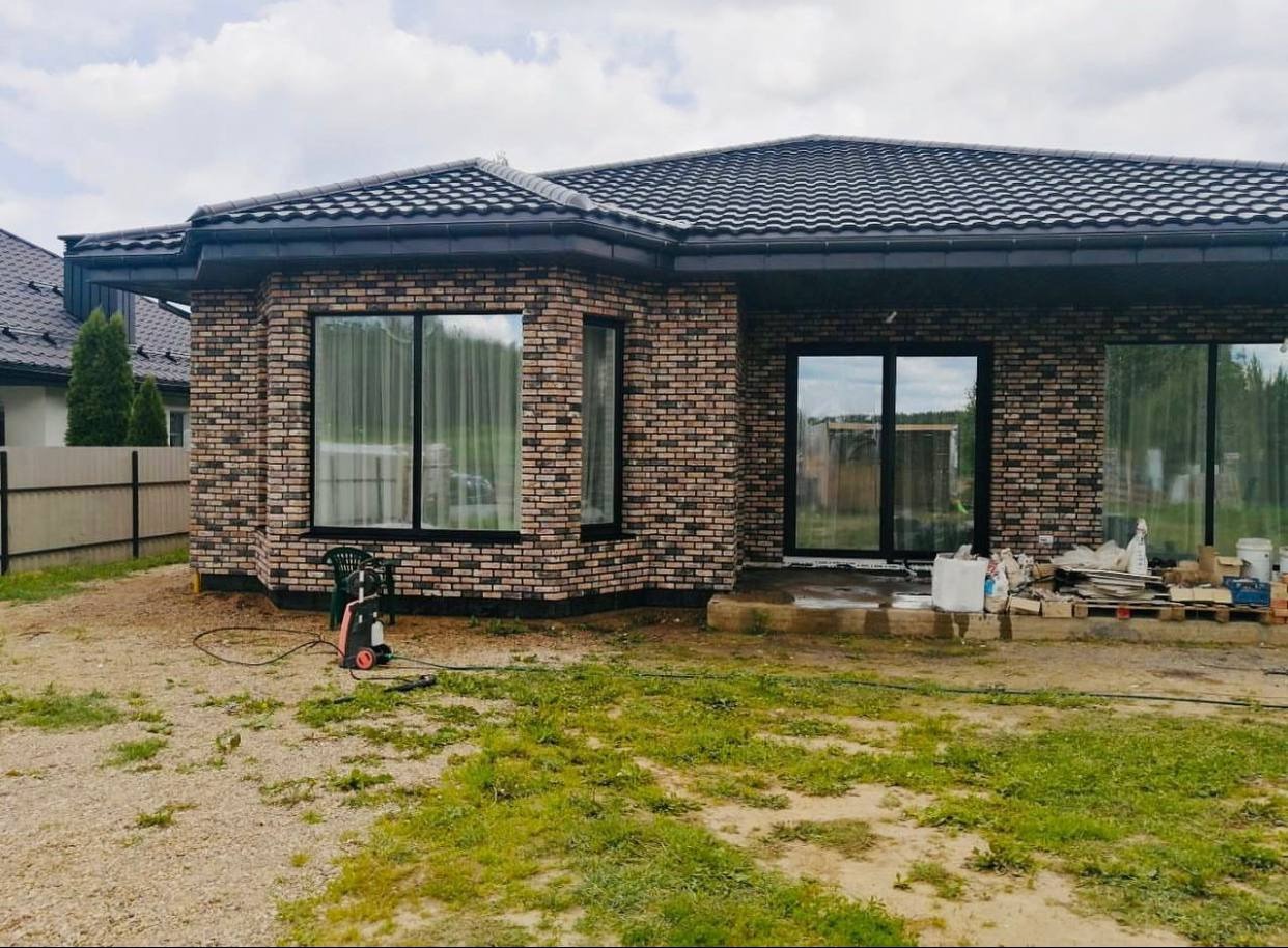 Nowo wybudowany dom z cegły klinkierowej z czarnymi oknami i dachem, na zewnątrz widoczny sprzęt do czyszczenia ciśnieniowego i materiały budowlane.