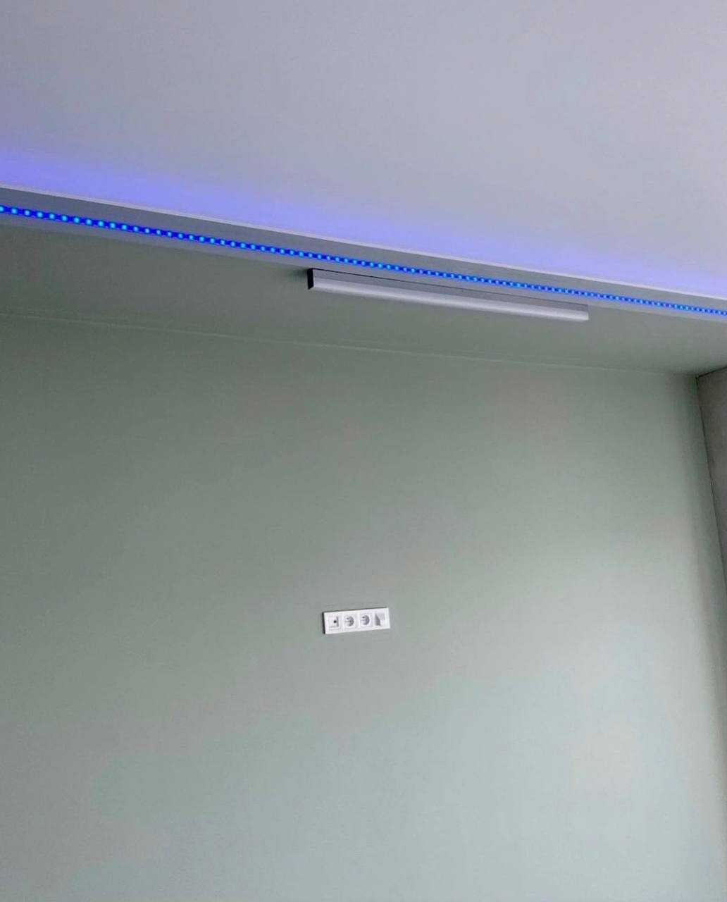 Ściana w odcieniu szaro-zielonym z zamontowanym oświetleniem LED w listwie podsufitowej, widoczne gniazdka elektryczne