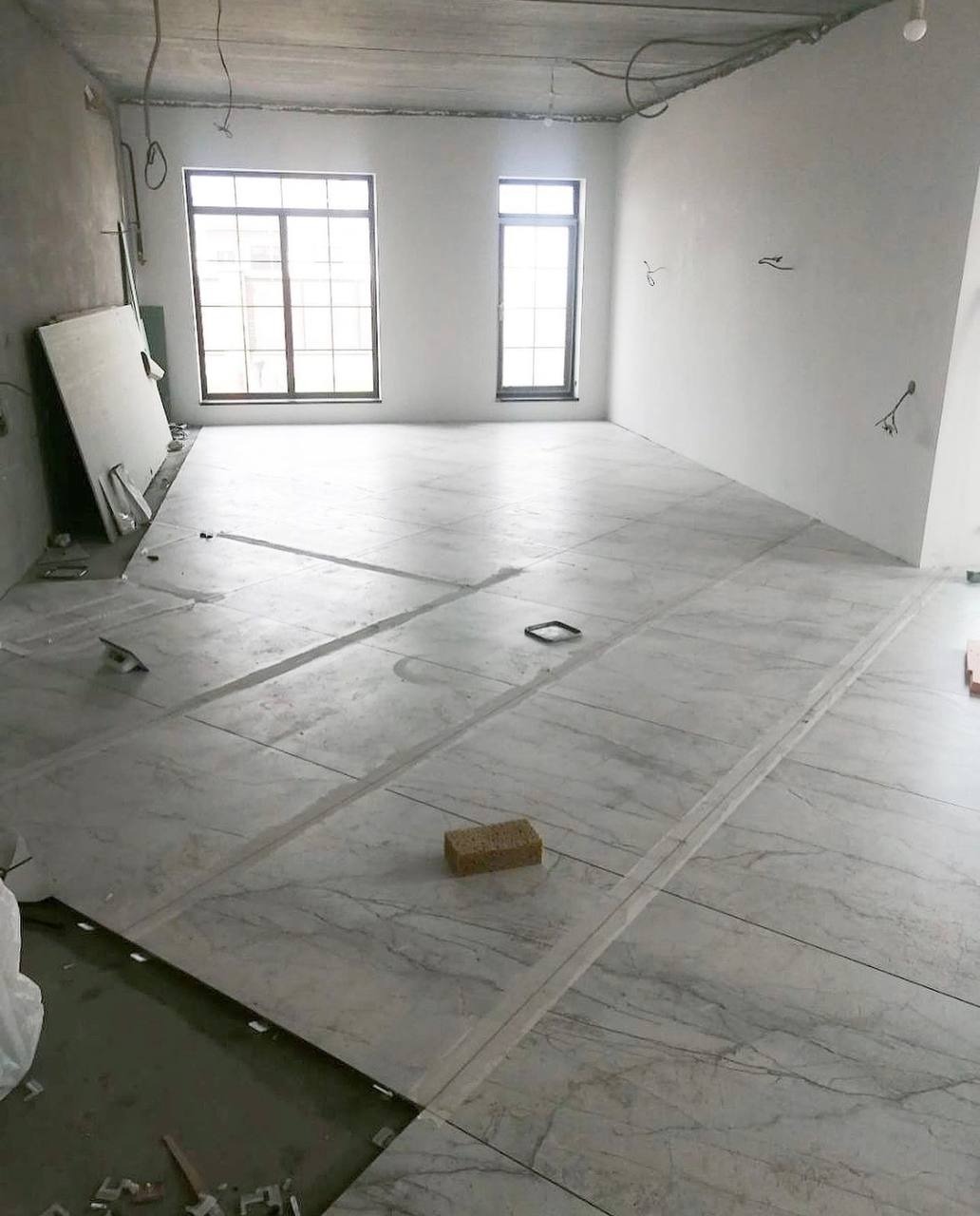 Układanie marmurowych płytek podłogowych w nowym mieszkaniu, widoczne listwy dystansowe i gąbka do czyszczenia fug.