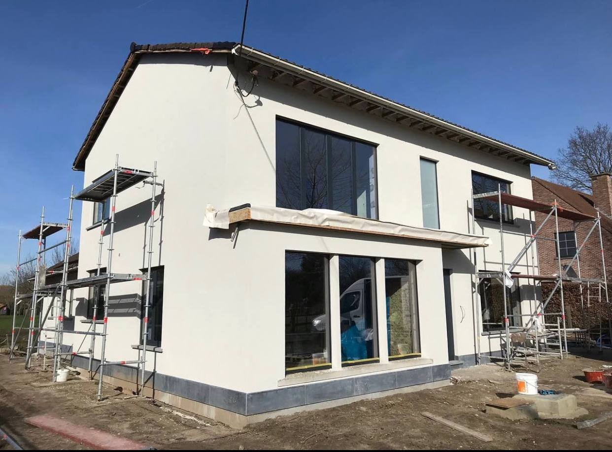 Dom z nową, jasną elewacją w trakcie prac wykończeniowych, widoczne rusztowania i zabezpieczenia okien.