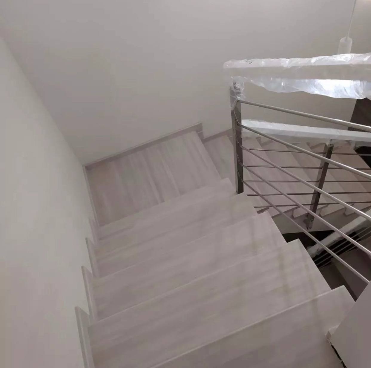 Wykończone schody z jasnego drewna z metalową barierką, zabezpieczoną folią ochronną, widok z góry.