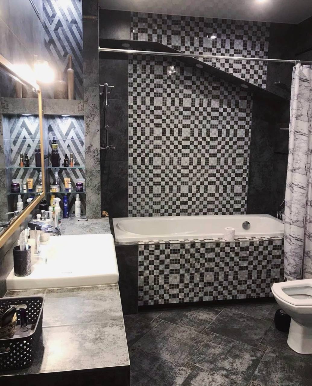 Nowoczesna łazienka w odcieniach szarości z mozaikową ścianą nad wanną, minimalistyczna umywalka z lustrem i półkami z kosmetykami.