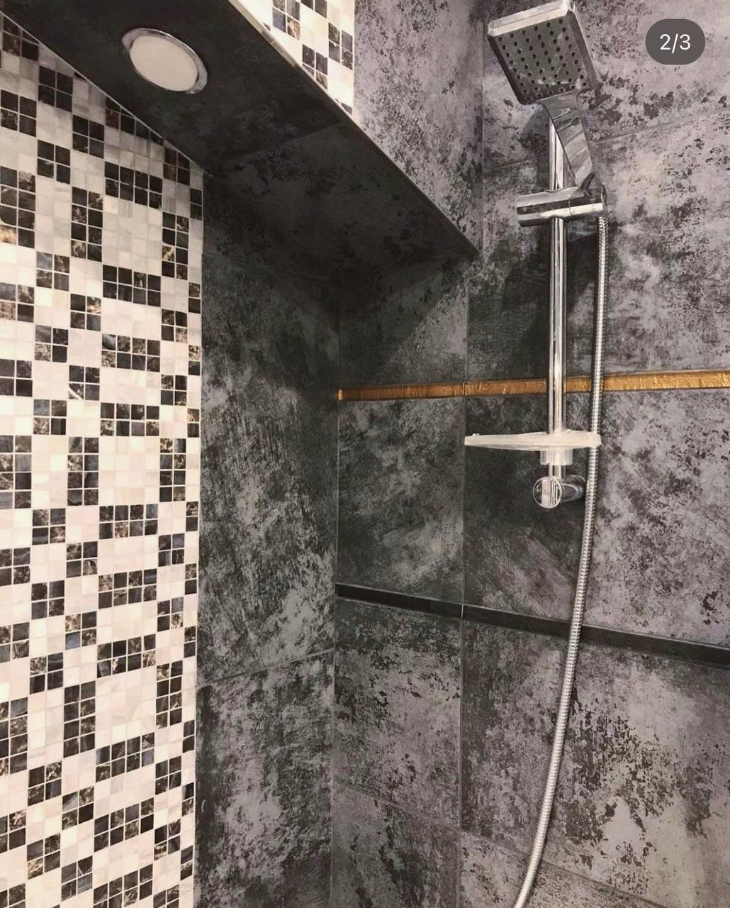 Nowoczesna kabina prysznicowa z szarą płytką imitującą beton, akcentująca złotą listwą, oraz ścianą wyłożoną mozaiką w szachownicę, oświetlona ledowym punktem.