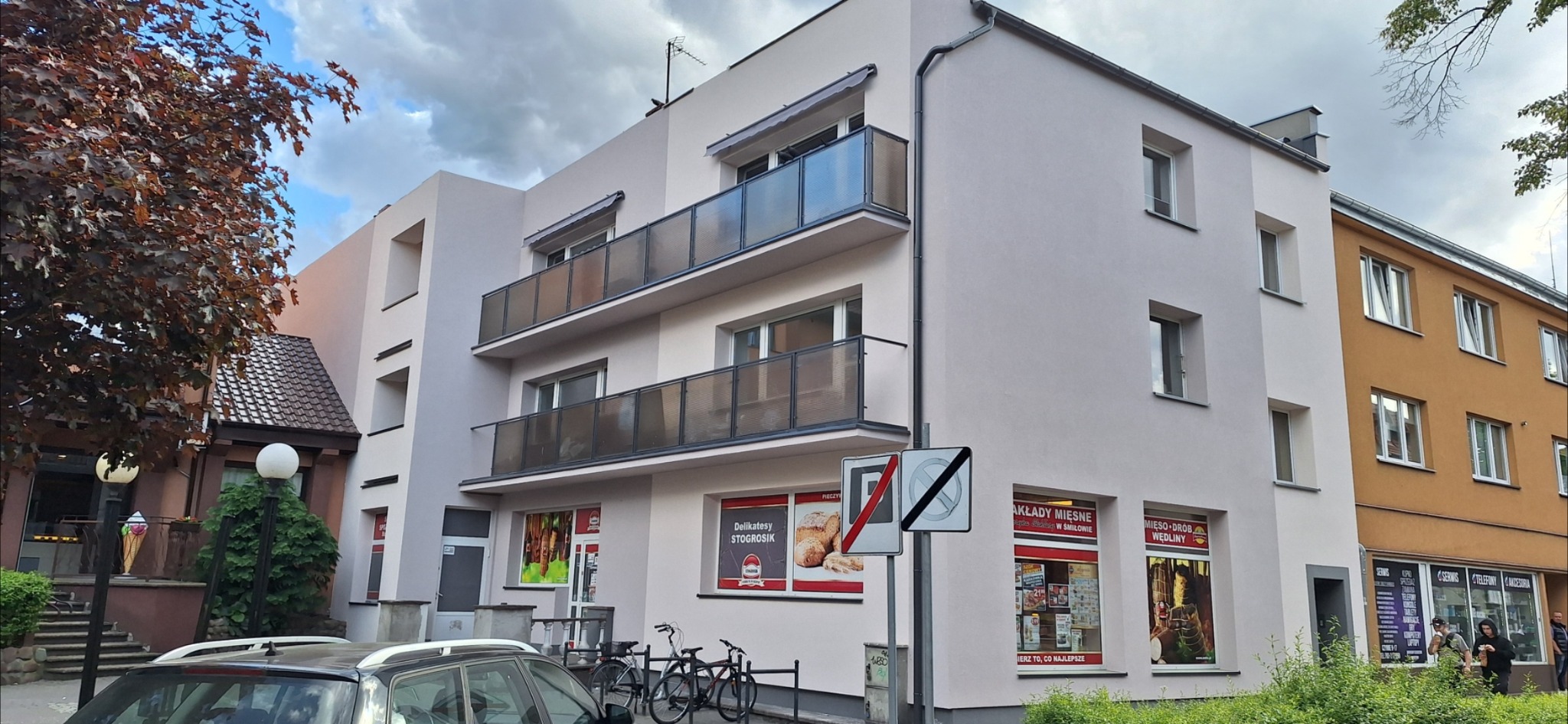 Elewacja budynku po remoncie z balkonami i oknami. Jasna kolorystyka, widoczne detale wykończenia. Ujęcie z poziomu ulicy, z elementami otoczenia miejskiego.