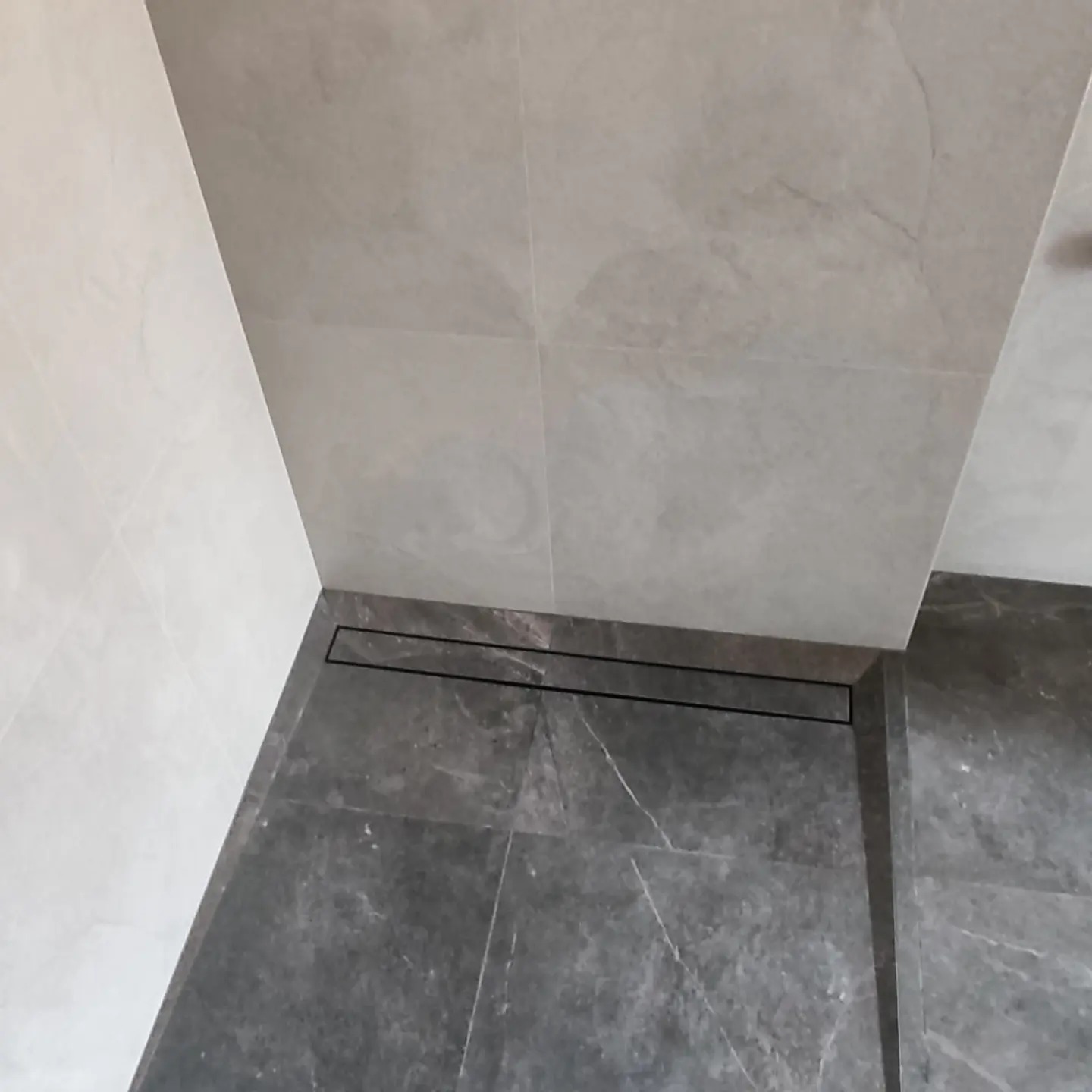 Szare płytki podłogowe i ścienne w łazience z odpływem liniowym, widok z góry.